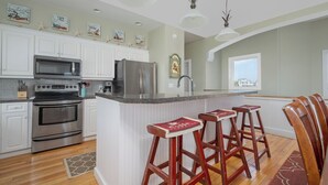 Una cocina con gabinetes blancos, electrodomésticos de acero inoxidable, encimera de granito y taburetes de madera.