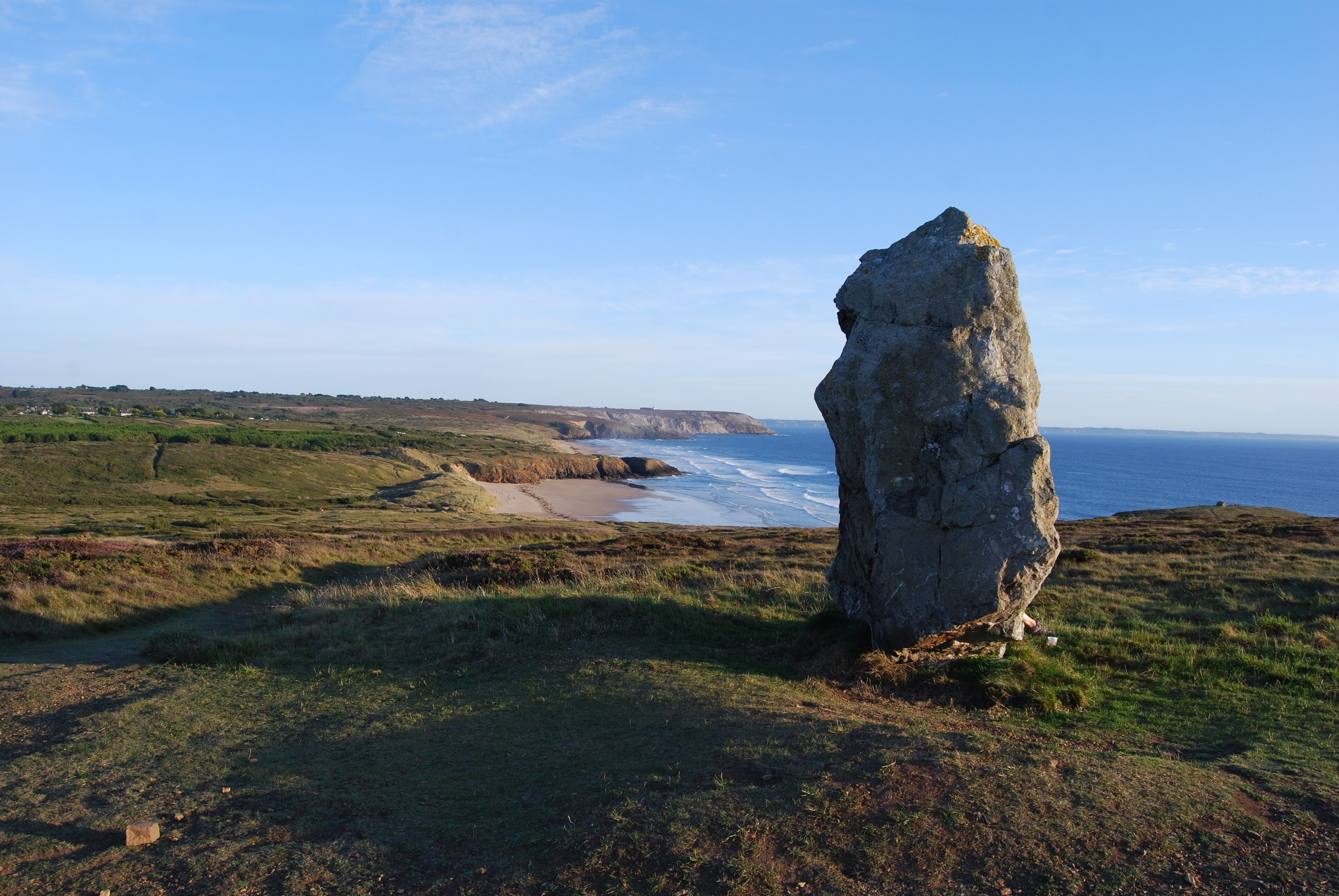 A coastal landscape with a prominent rock formation, a sandy beach, and a view of the sea.