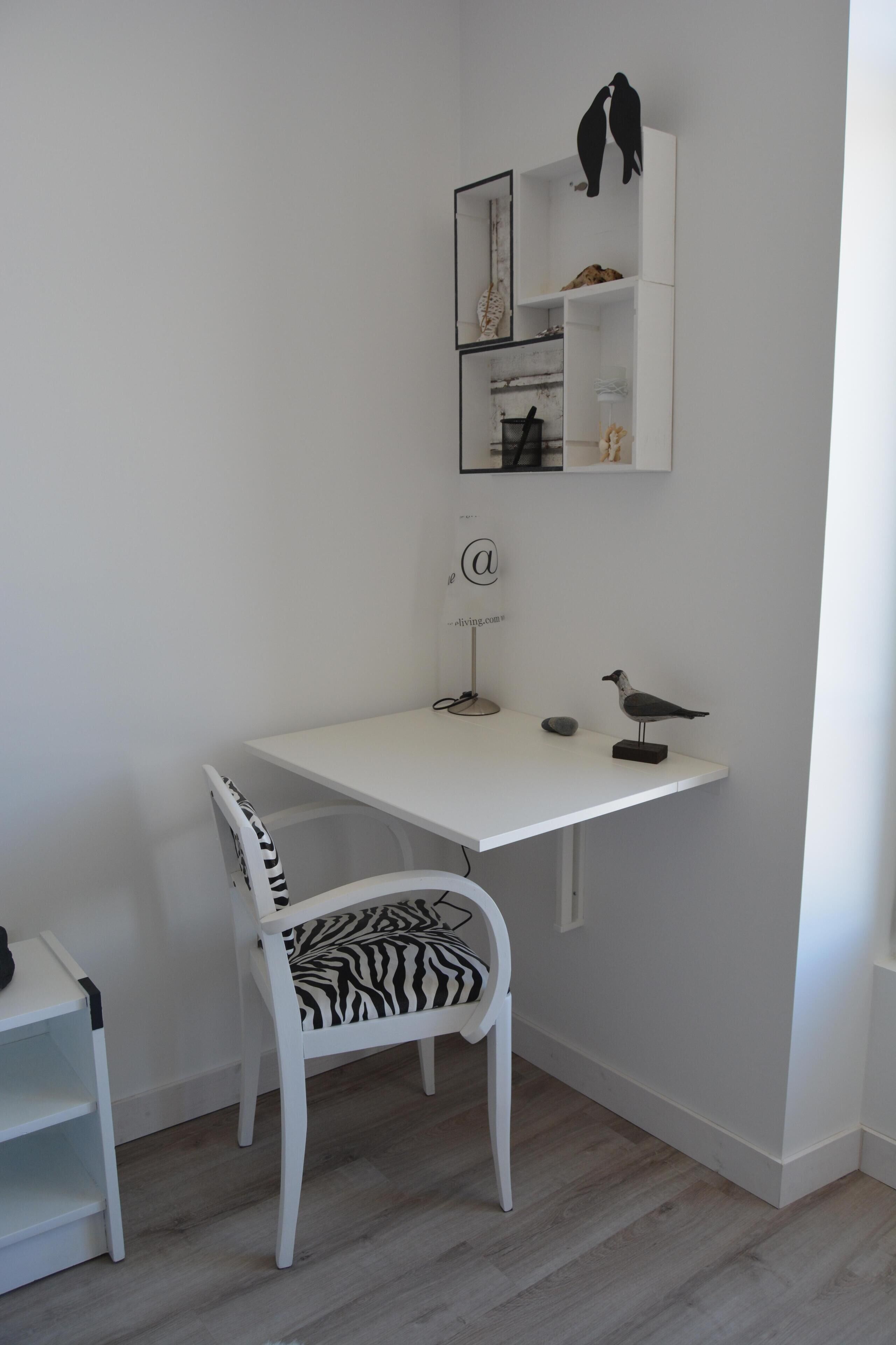 Un bureau blanc avec une chaise à motifs zébrés, une petite étagère ornée d’objets décoratifs et une étagère murale sur laquelle sont posées deux figurines d’oiseaux.
