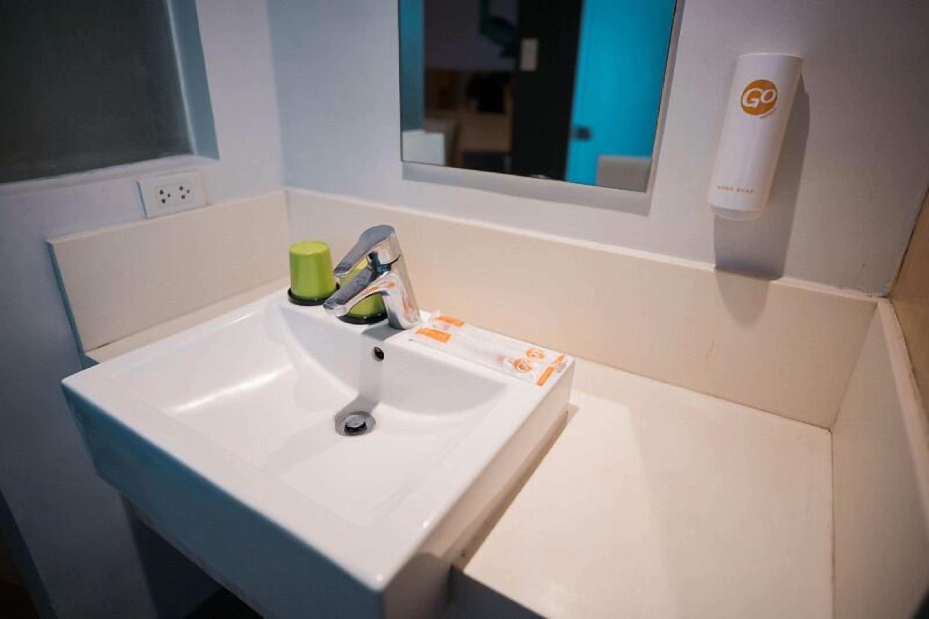 A white bathroom sink with a mirror above it, a green soap dispenser, and a Go product on the wall.