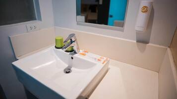 A white bathroom sink with a mirror above it, a green soap dispenser, and a Go product on the wall.