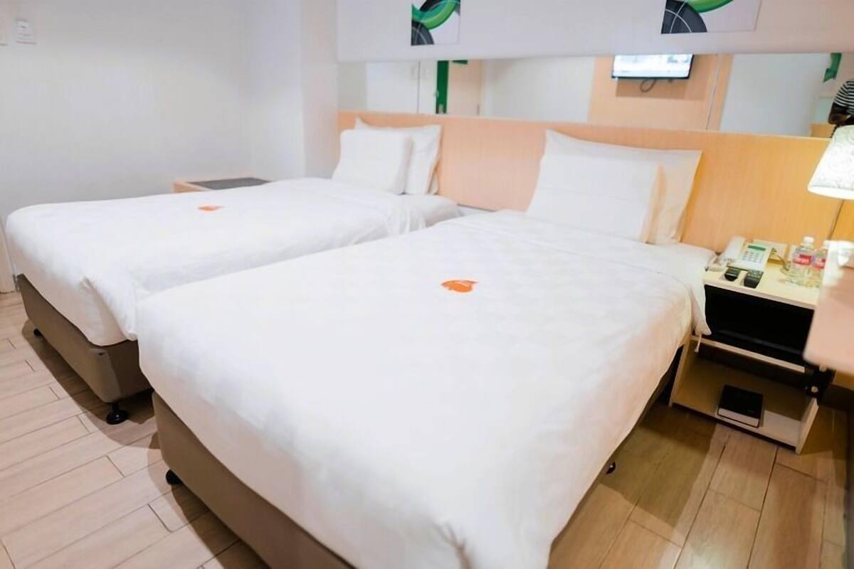 A hotel room with two beds, a nightstand, a lamp, and a small table with a phone and toiletries.