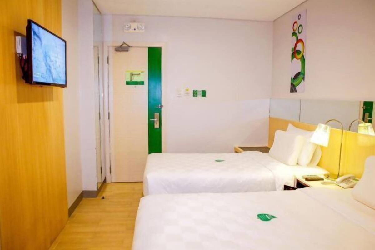 A hotel room with two beds, a TV, a desk with a lamp, and a green door.