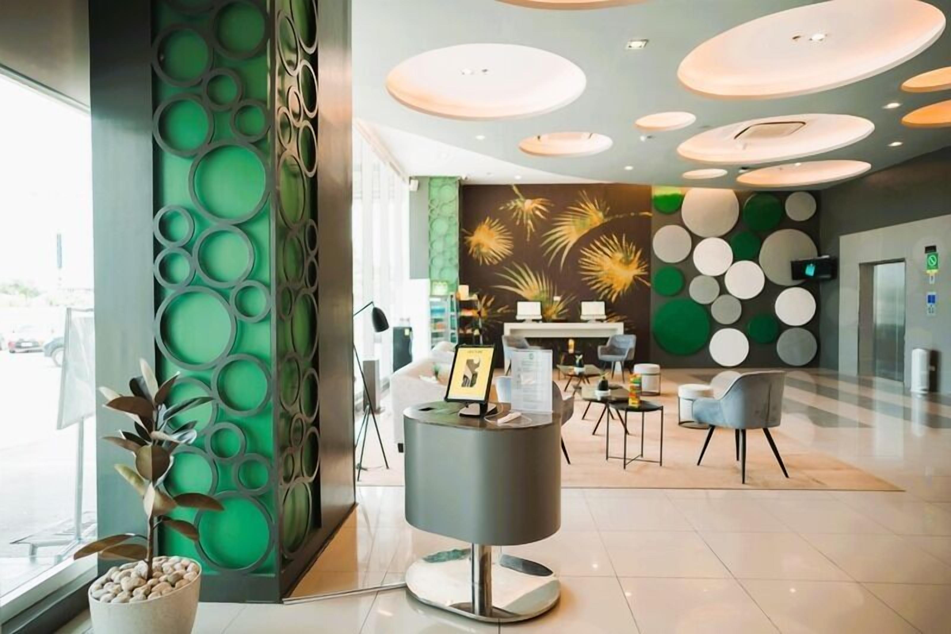 A modern lobby with a reception desk, seating area, decorative wall panels, and a large window.