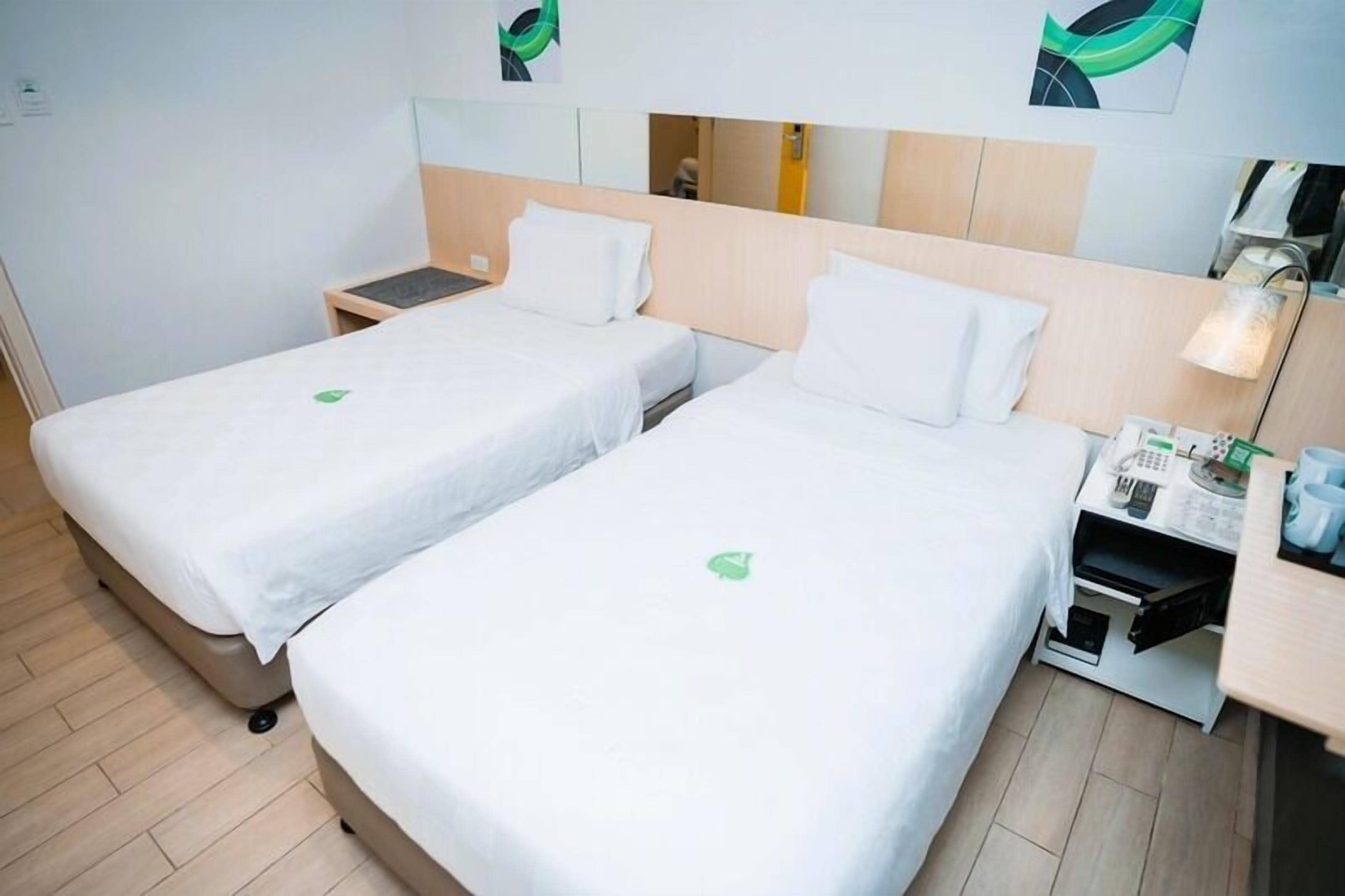 Camera d'albergo con due letti, un comodino, una lampada e un tavolino con un telefono e dei documenti.