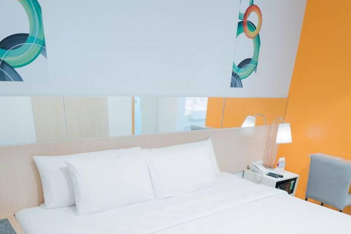 A neatly made bed with white bedding, a bedside table with a lamp, and a chair.