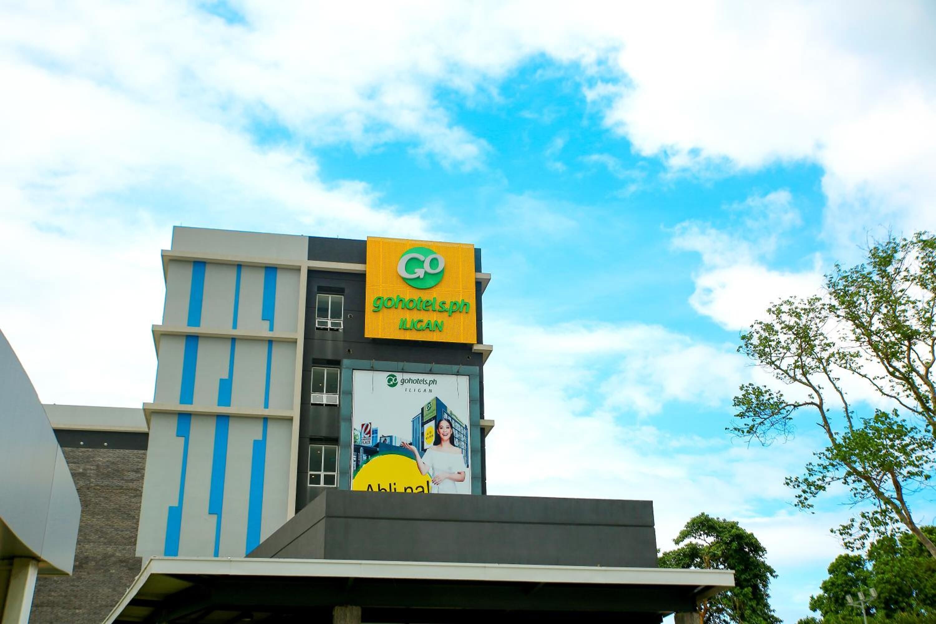 A modern building with a prominent GoHotels.ph sign, a large billboard advertising the hotel, and a clear blue sky in the background.