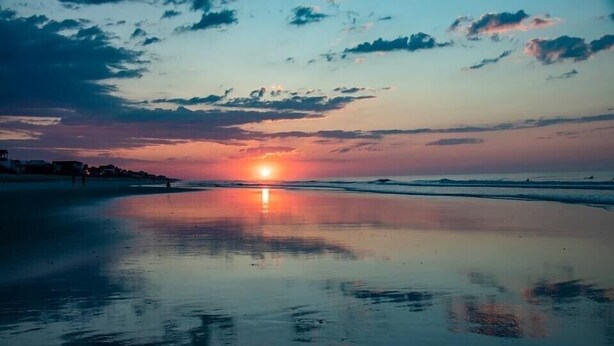 Une plage au coucher du soleil, avec des eaux calmes qui reflètent le ciel.