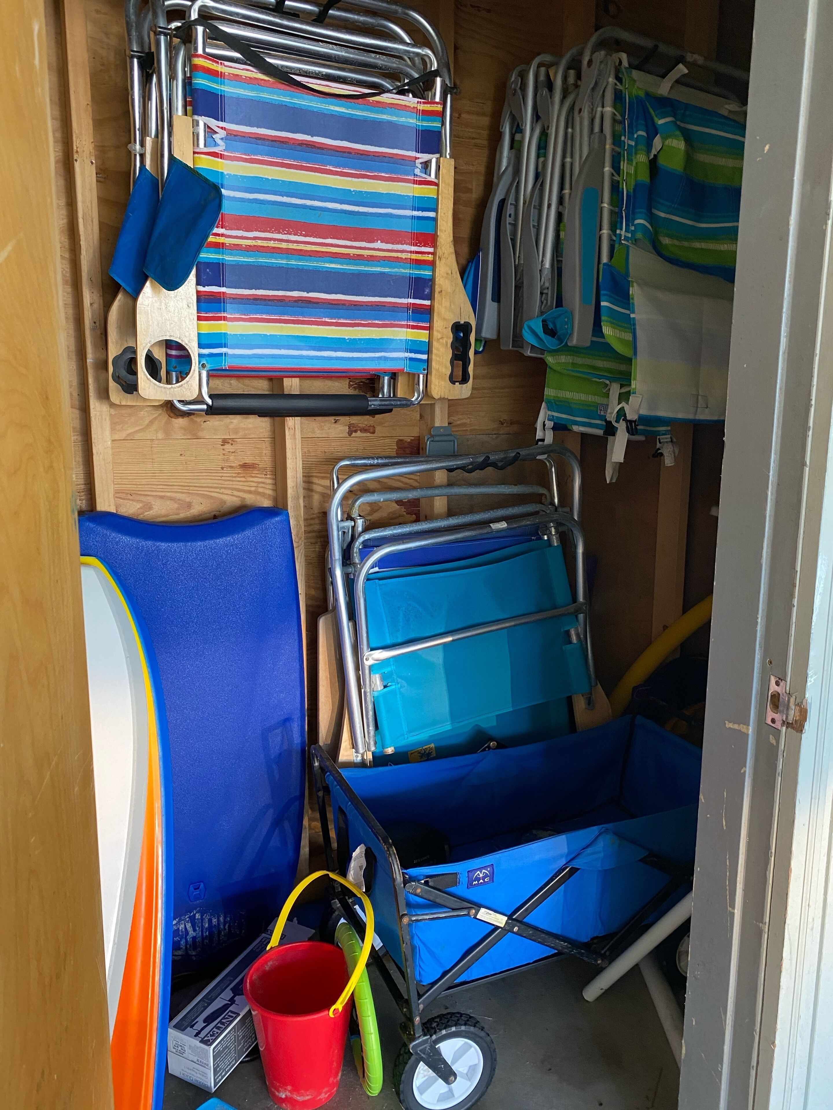 A compact storage area with metal racks holding striped towels, a blue folding chair, and a blue cart with wheels.