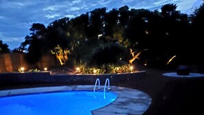 Une piscine à trois niveaux, entourée d’une terrasse en béton et d’arbres.