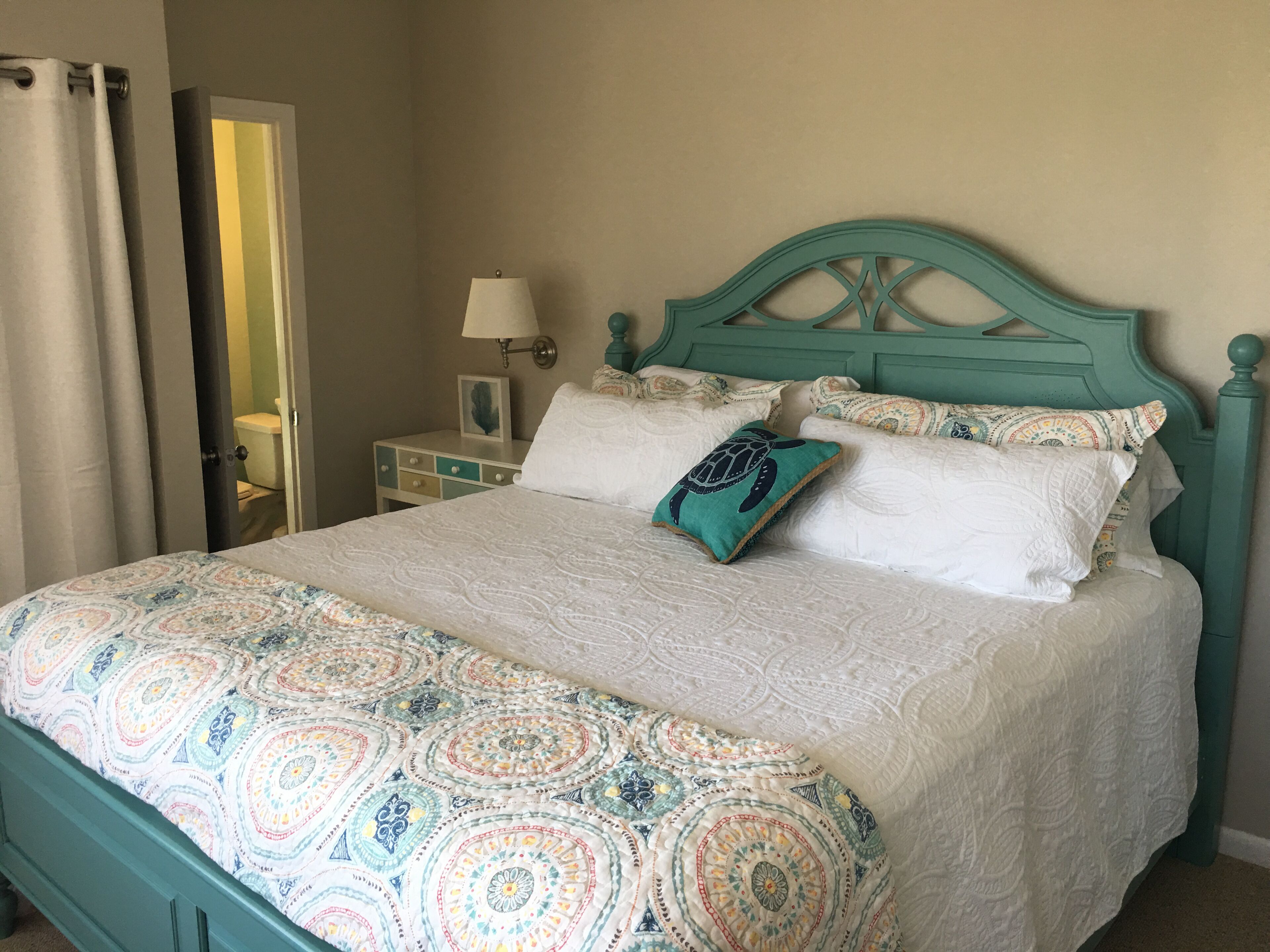 A bed with a patterned bedspread, a teal headboard, and a pillow with a turtle design.