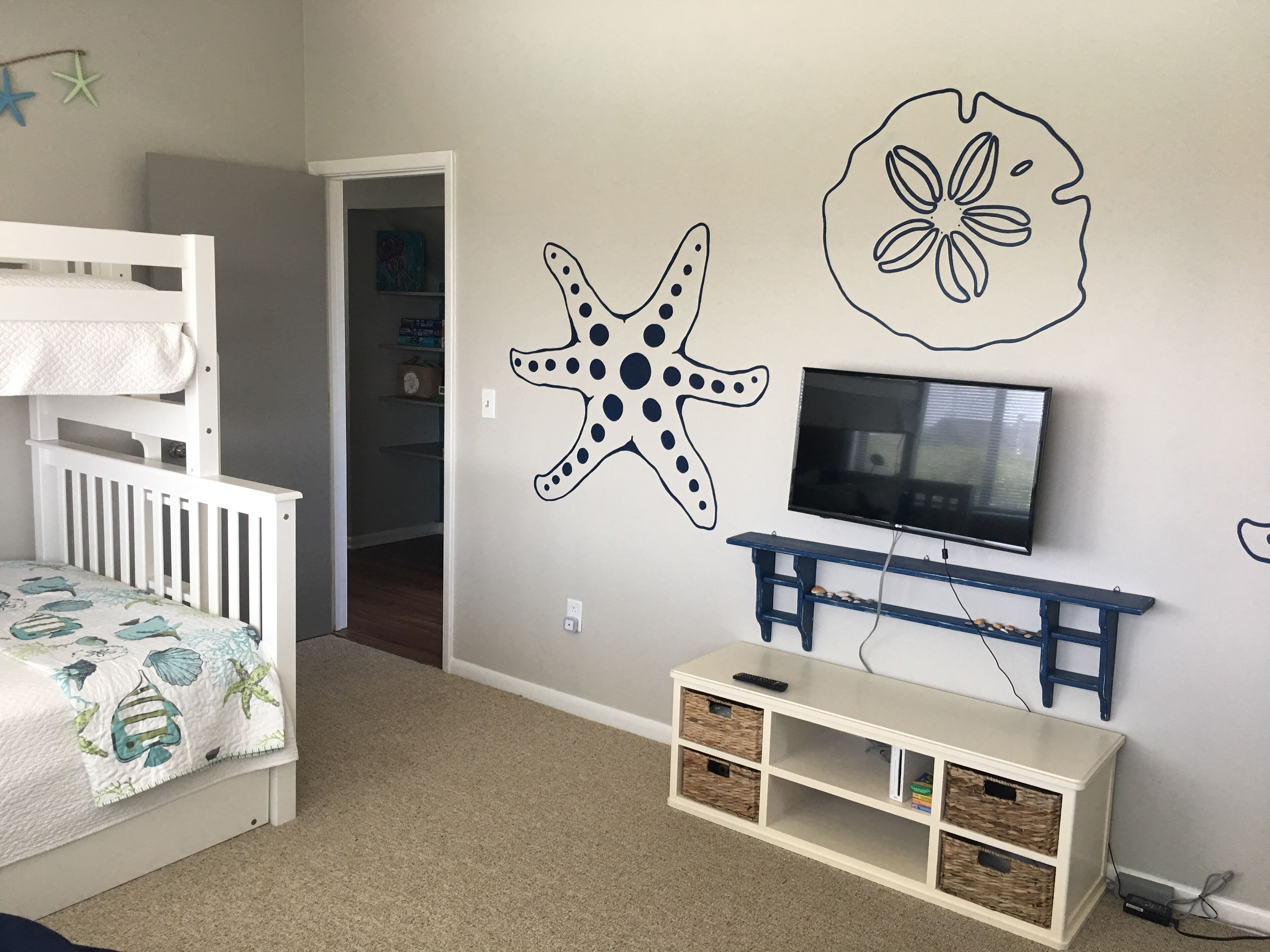A child's room with bunk beds, a TV, and a wall decorated with starfish and a flower.