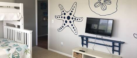 A child's room with bunk beds, a TV, and a wall decorated with starfish and a flower.