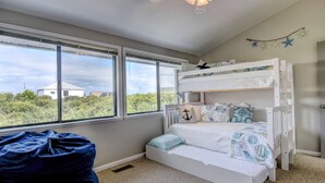 Une chambre avec un lit superposé, un fauteuil en forme de poire et une vue sur l’extérieur grâce à de grandes fenêtres.