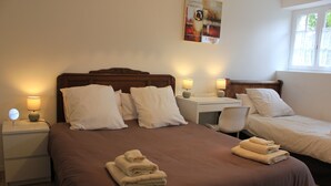 Quarto de hotel com uma cama grande, duas mesas de cabeceira com luminárias, uma escrivaninha e uma cadeira. Há toalhas na cama e um cartaz na parede.