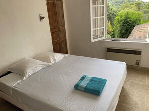 Ein Schlafzimmer mit Bett, einem Fenster mit Blick ins Grüne und einer Holztür.