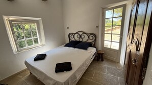 A bedroom with a bed, a window, a door, and a small stool.