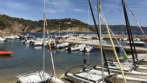 A marina with various boats docked, a rocky hillside in the background, and a clear sky.
