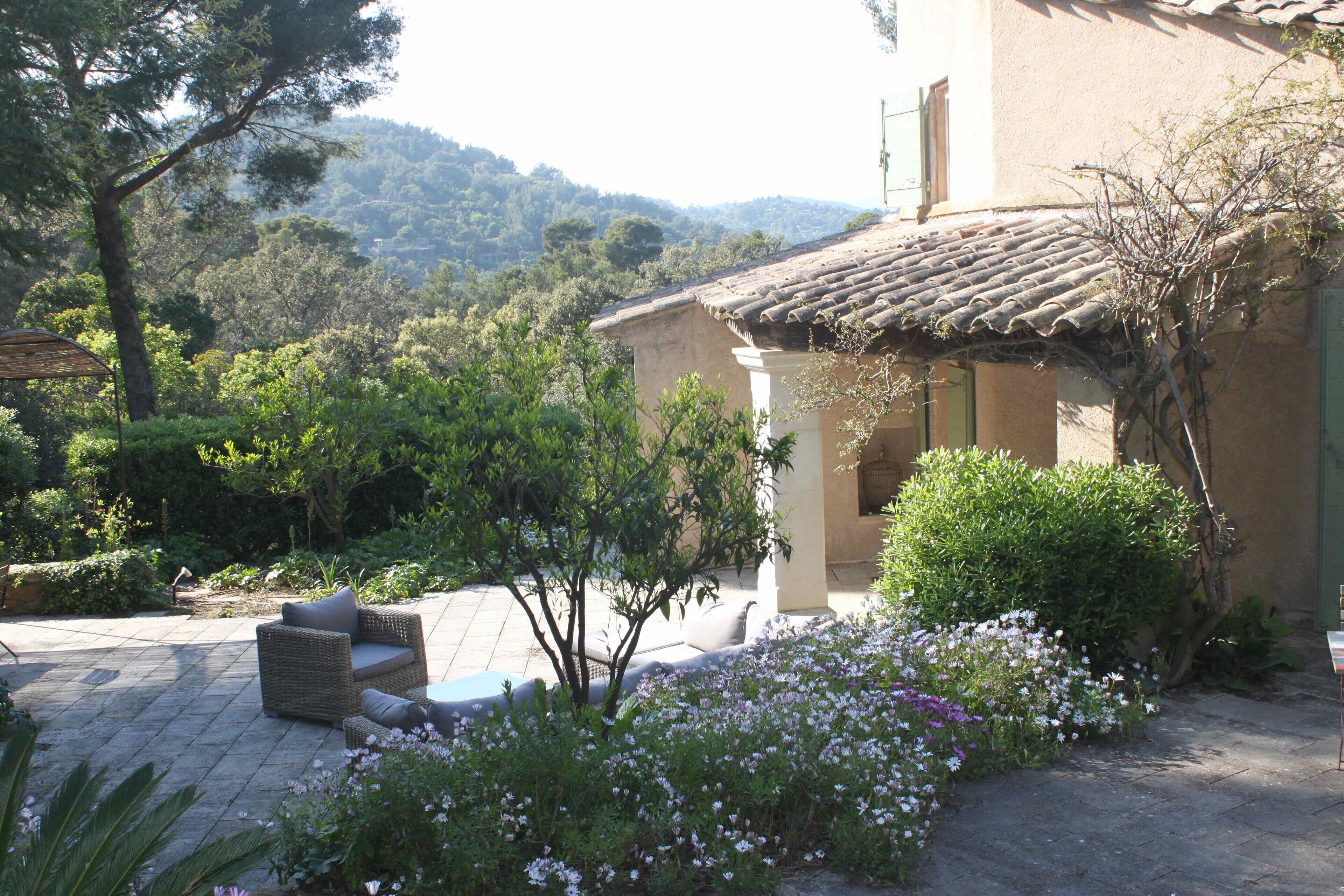 Una casa con techo de tejas, un jardín con flores y un patio con mobiliario.