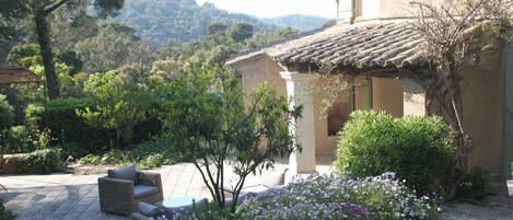 Una casa con techo de tejas, un jardín con flores y un patio con mobiliario.