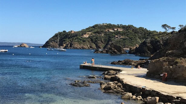 A coastal scene with clear waters, rocky shore, and a small pier.