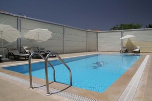 En swimmingpool med liggestole og parasoller, omgivet af et højt hegn.