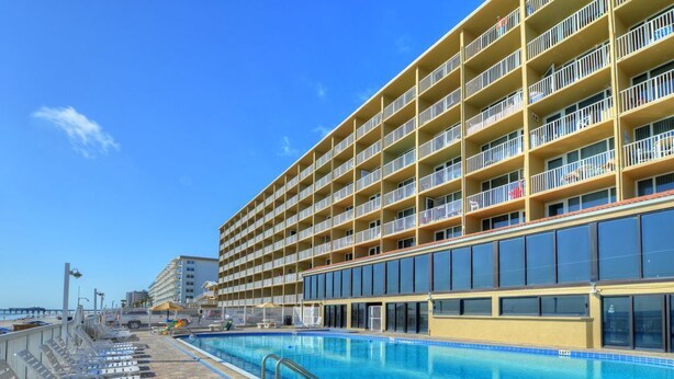 Um hotel com uma piscina grande, várias varandas e um céu azul límpido.