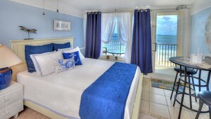Quarto com cama, mesa de cabeceira, mesa e cadeiras, e vista para o mar.