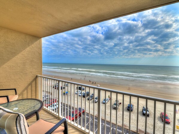 A balcony with a view of the beach and parked cars. - Oceanfront Condo | Hidden Treasure @ Pirates Cove (Daytona Beach)