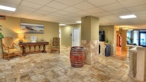 Um hall com piso de pedra, um banco de madeira, um barril redondo e uma pintura na parede.