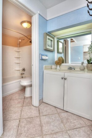 A bathroom with a toilet, a shower, and a vanity with a mirror. - Oceanfront Condo | Hidden Treasure @ Pirates Cove (Daytona Beach)