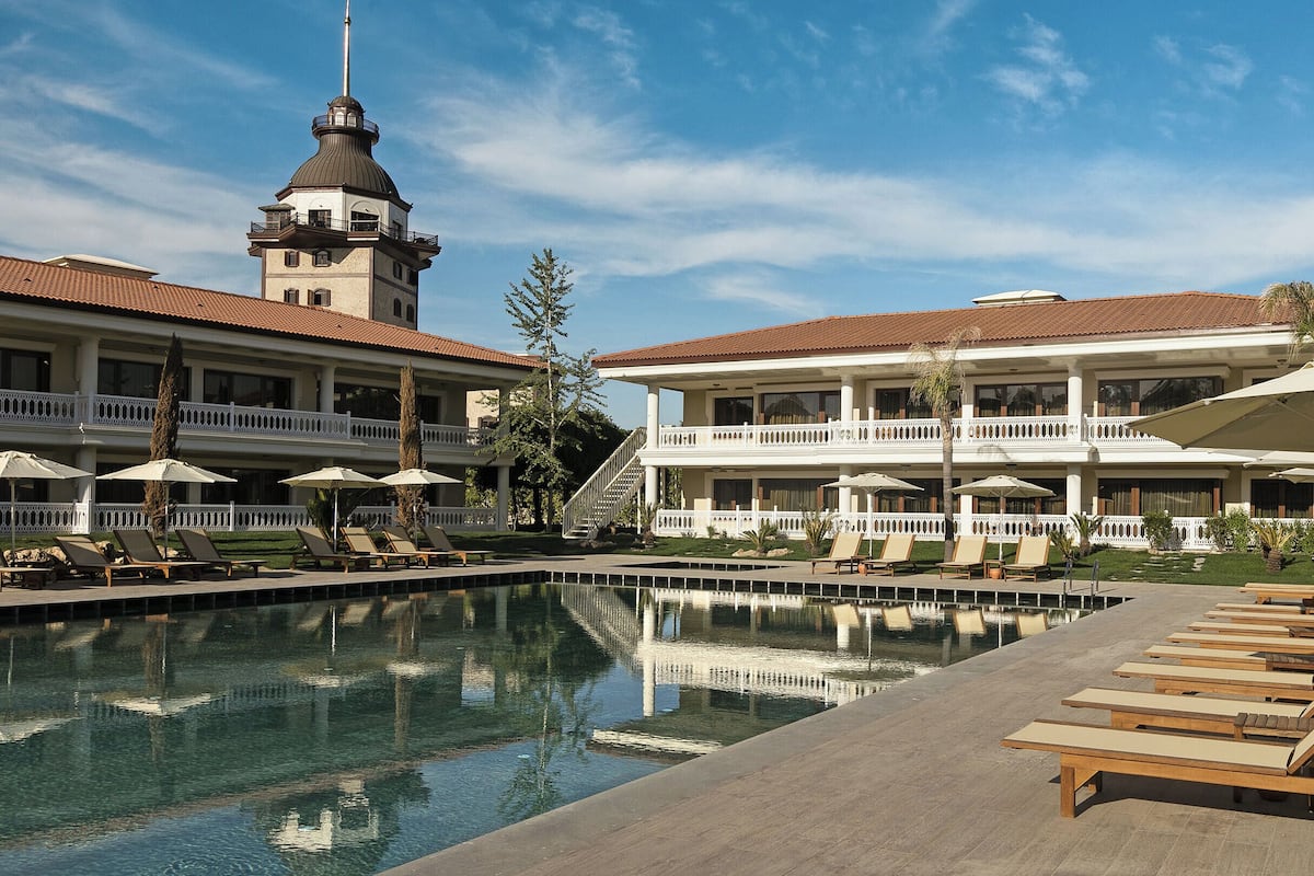 A hotel with a swimming pool, lounge chairs, and umbrellas.