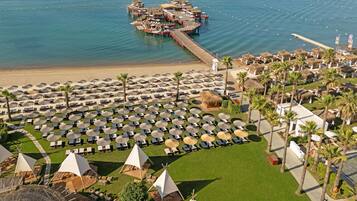 An aerial view of a resort with multiple beachside umbrellas, lounge chairs, and thatched-roof structures.