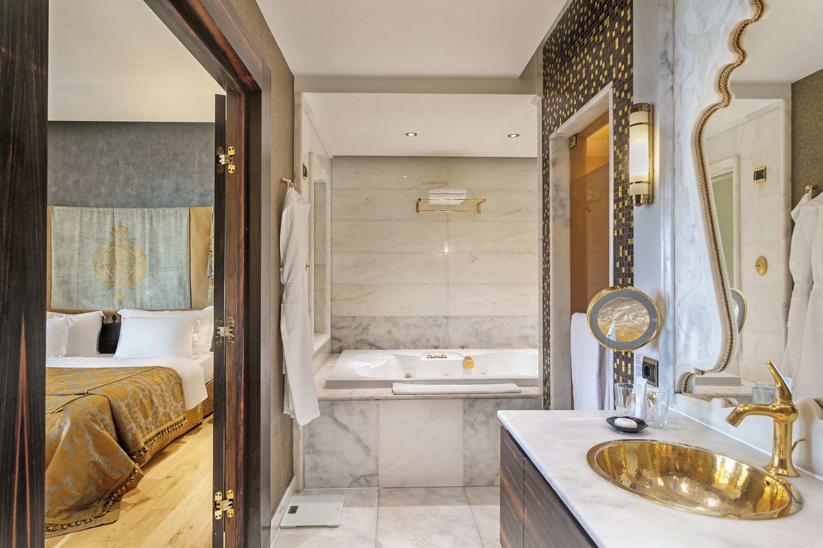 A modern bathroom with a gold sink, a bathtub, and a large mirror.