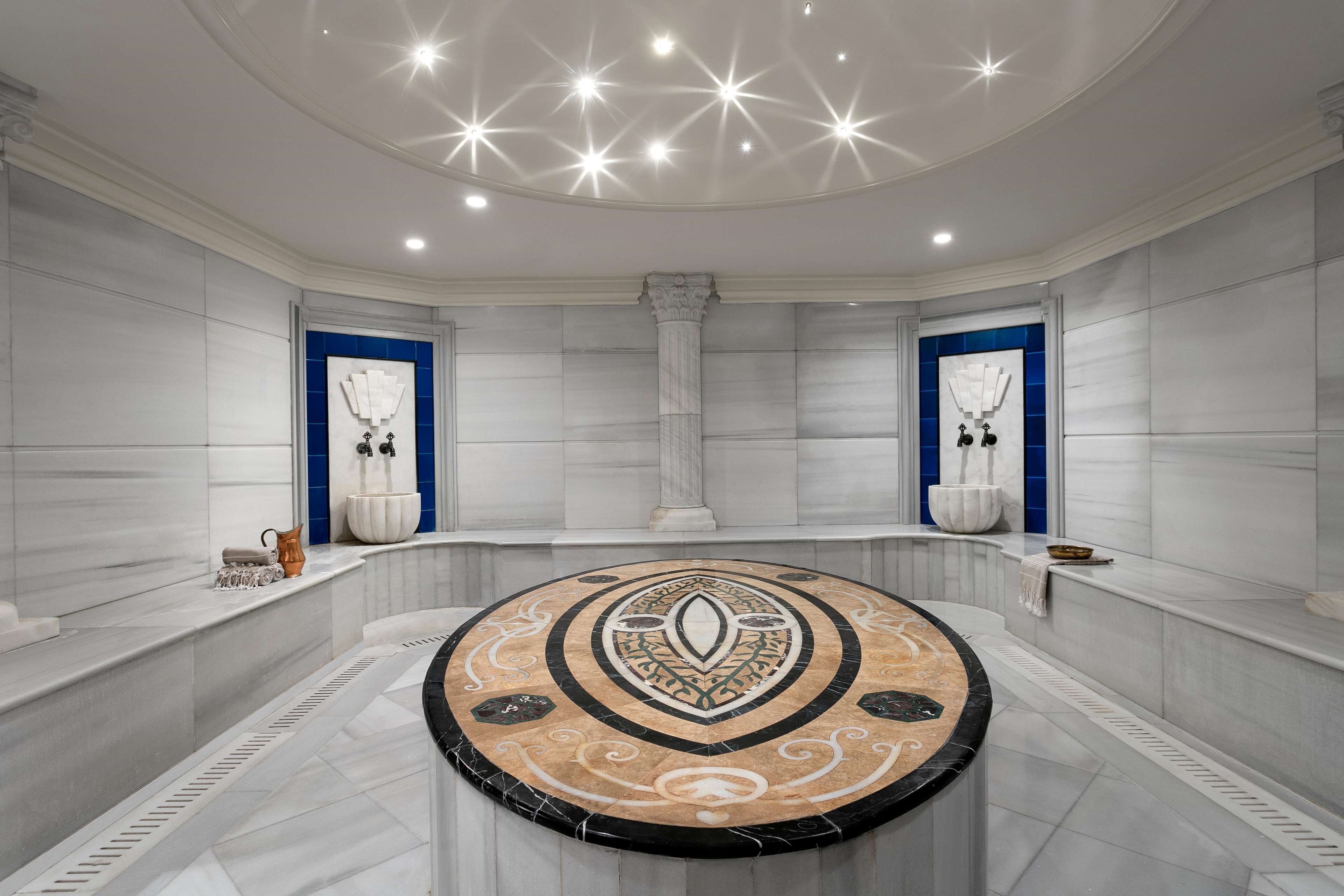 Un baño lujoso con un diseño circular en el suelo, paredes de mármol y dos puertas con marcos azules.