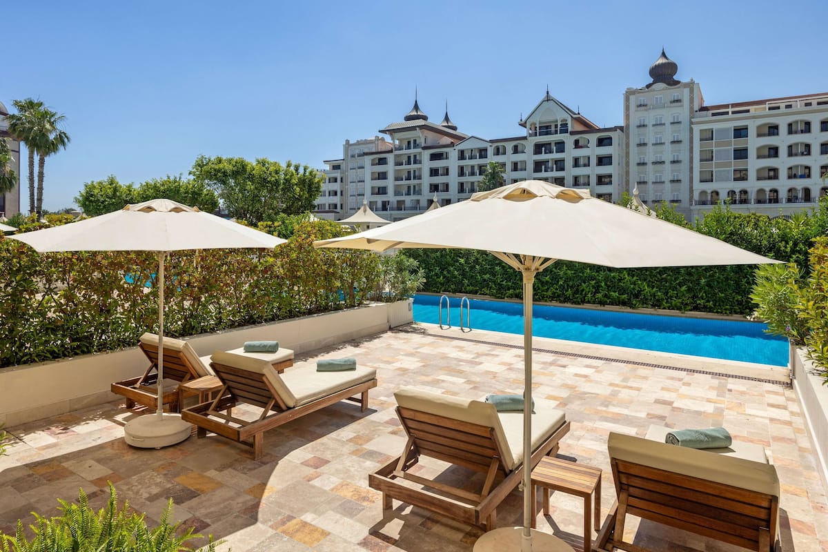 A rooftop pool area with lounge chairs and umbrellas, a swimming pool, and a view of hotel buildings in the background.