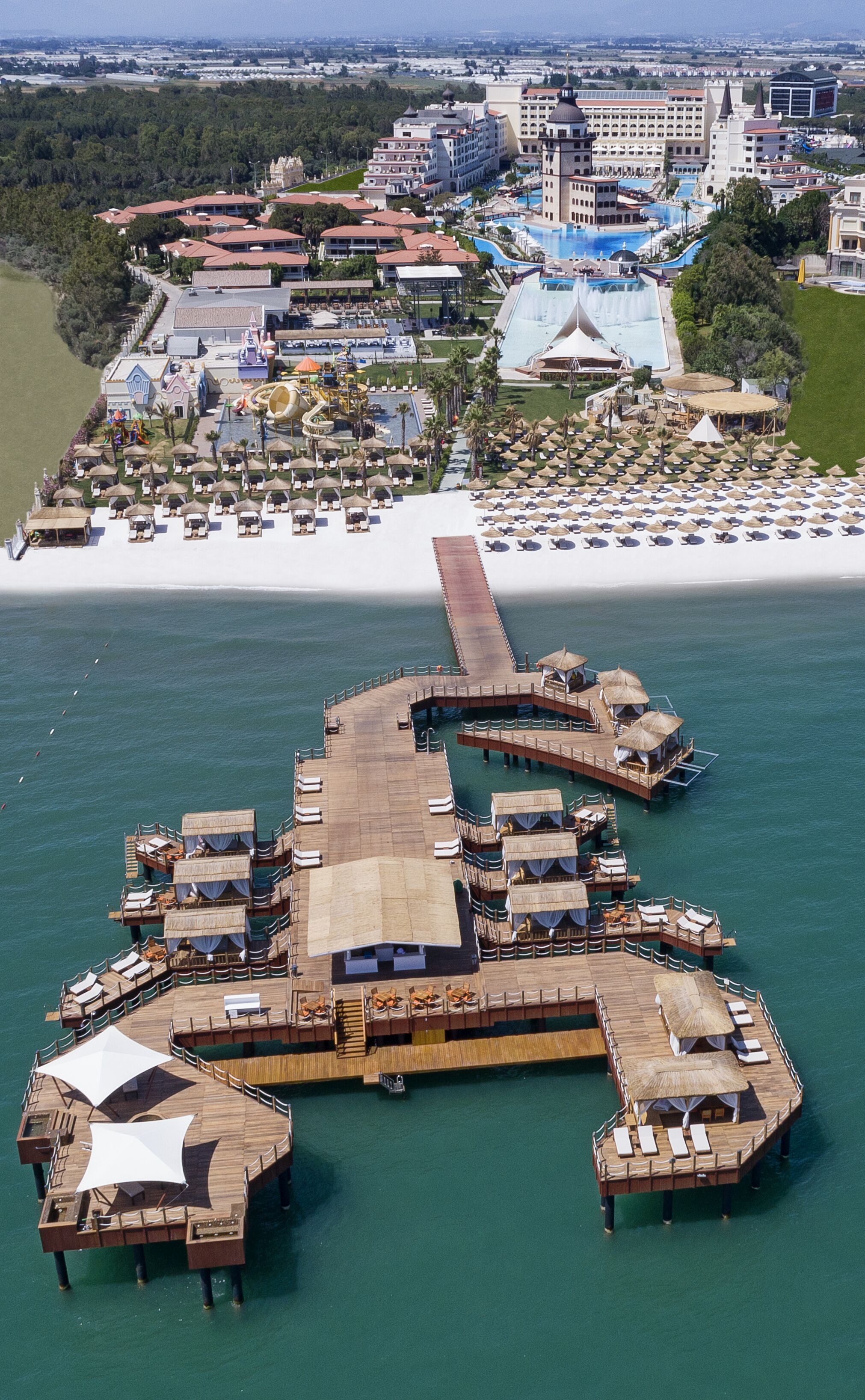 An aerial view of a resort with a large pool, multiple buildings, and a pier extending into the water.