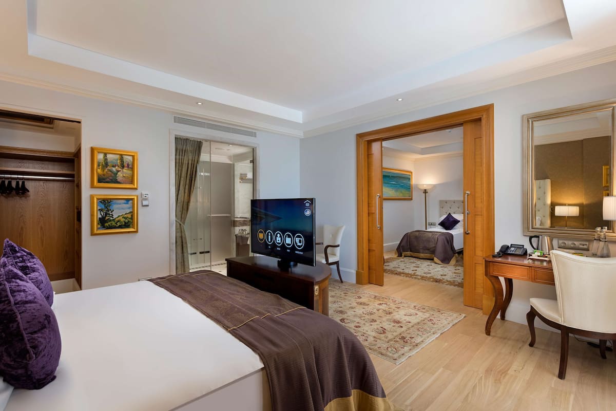 A hotel room with a bed, a desk, a chair, a television, and a door leading to another room.