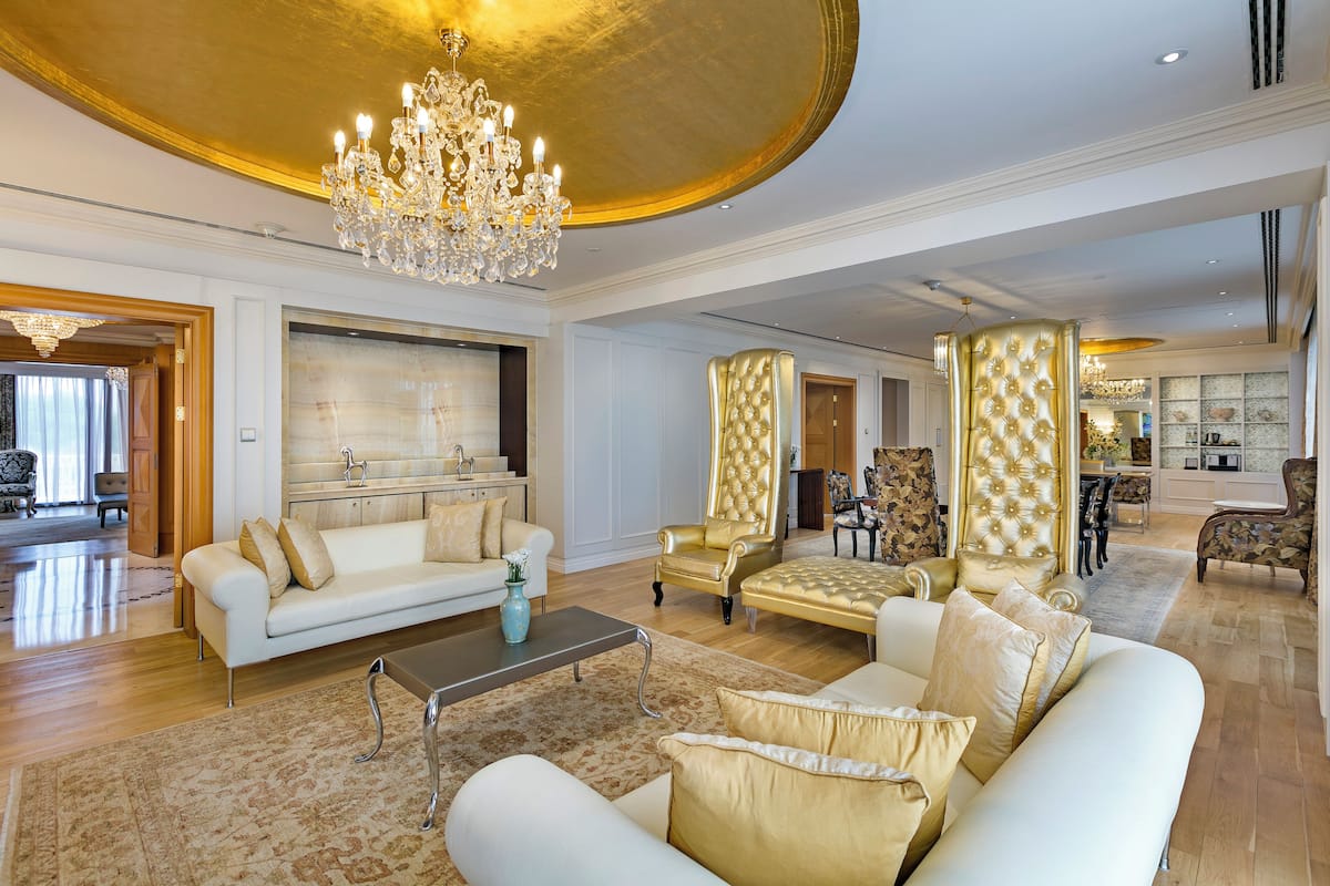A spacious living room with a white sofa, a gold armchair, and a chandelier.