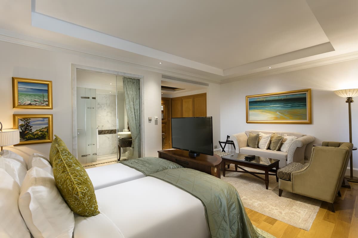 A hotel room with a large bed, a sofa, a television, and artwork on the walls.