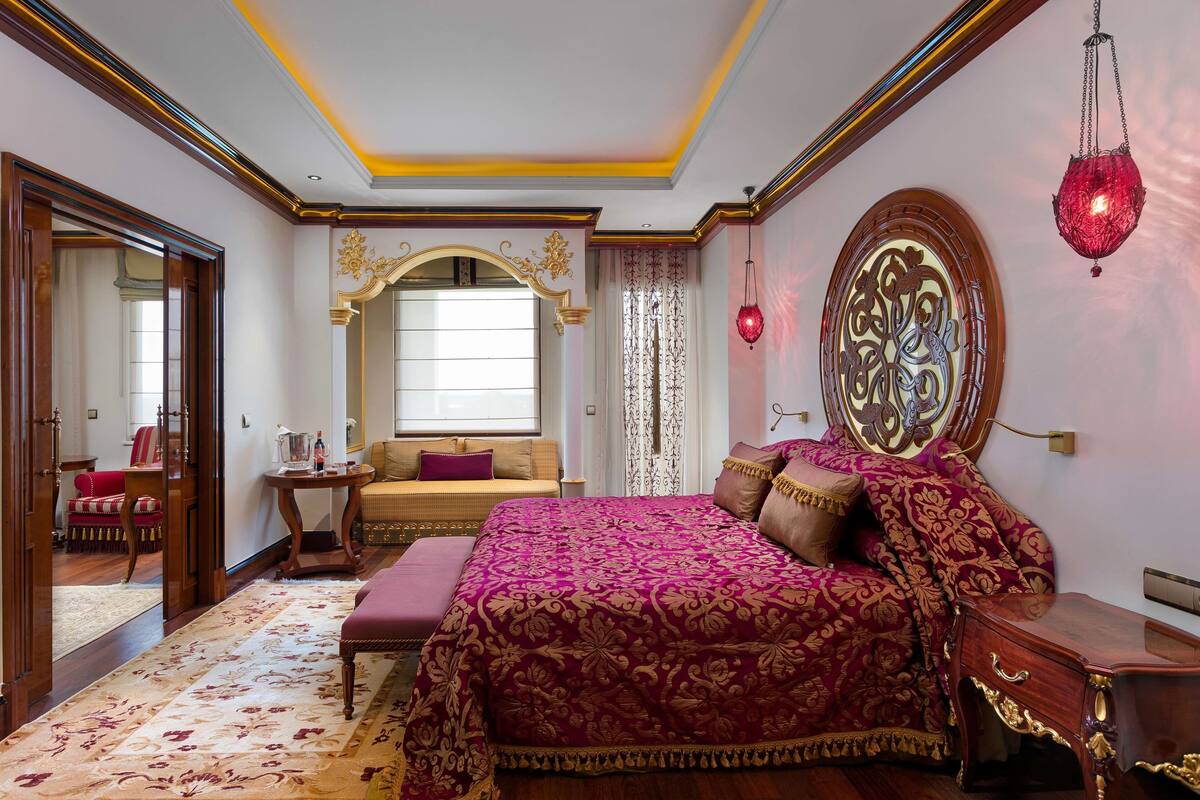 A bedroom with a large bed, a bedside table, a hanging red lantern, and a mirror with an ornate frame.