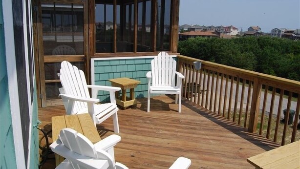 Una terraza de madera con dos sillas Adirondack blancas y una mesita.