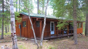 Une cabane en bois dotée d’un porche, entourée d’arbres.