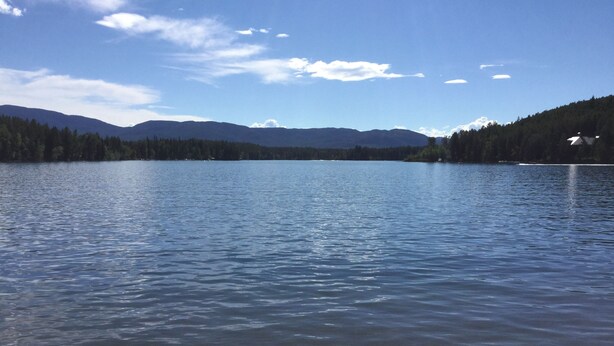 Un lac paisible, avec des montagnes en arrière-plan et un ciel dégagé.