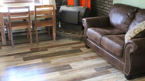 Un salon avec un canapé en cuir marron, des chaises en bois, une cheminée en pierre et un mur en briques.