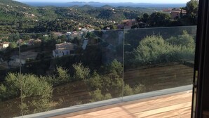 A balcony with a view of a hilly landscape, including houses and trees.