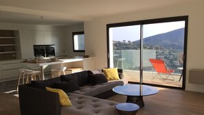 A modern living room with a sectional sofa, a glass dining table, and a balcony with a chair.