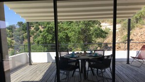 A balcony with a table and chairs, overlooking a mountainous landscape.