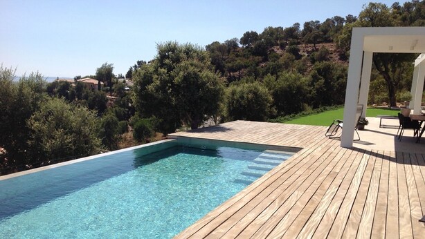 A rectangular swimming pool with clear blue water, surrounded by a wooden deck.