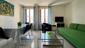 Una sala de estar moderna con un sofá verde, una mesa de centro de vidrio, un comedor con mesa y sillas, un televisor y un cuadro en la pared.